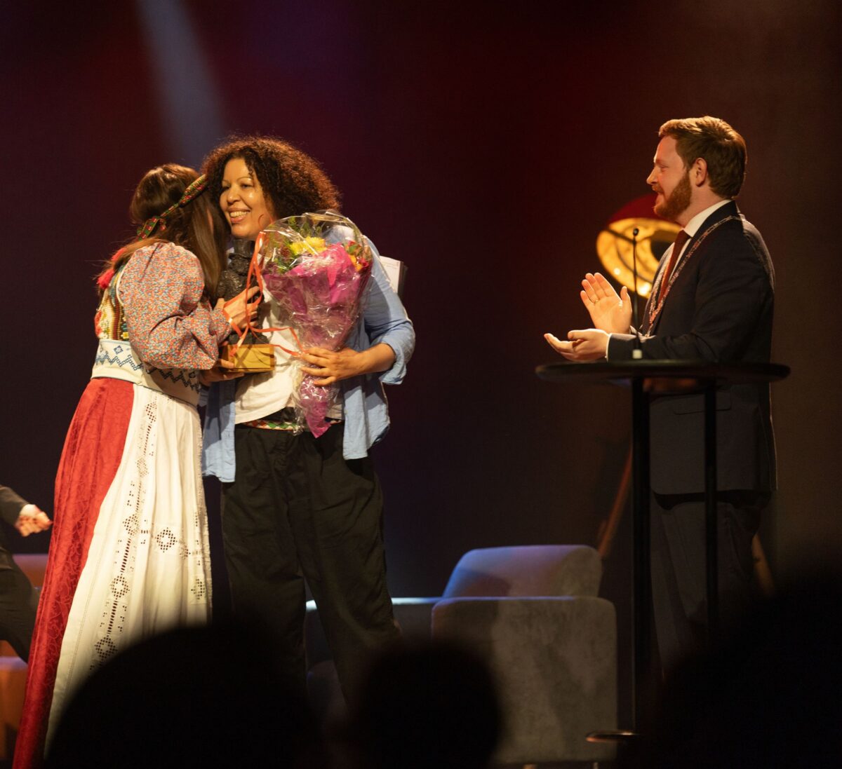 Prisvinner gratuleres med blomsterkrans. På bildet: Charlotte Frogner, Linda Gathu og Ordfører Marius Roheim Aarvold